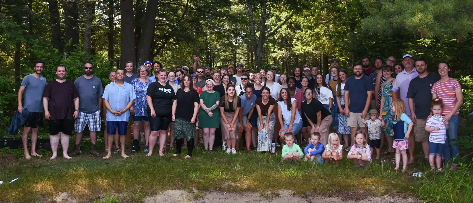 The His Mansion community, dozens of adults and children, gathered for a group photo among tall pines in summer