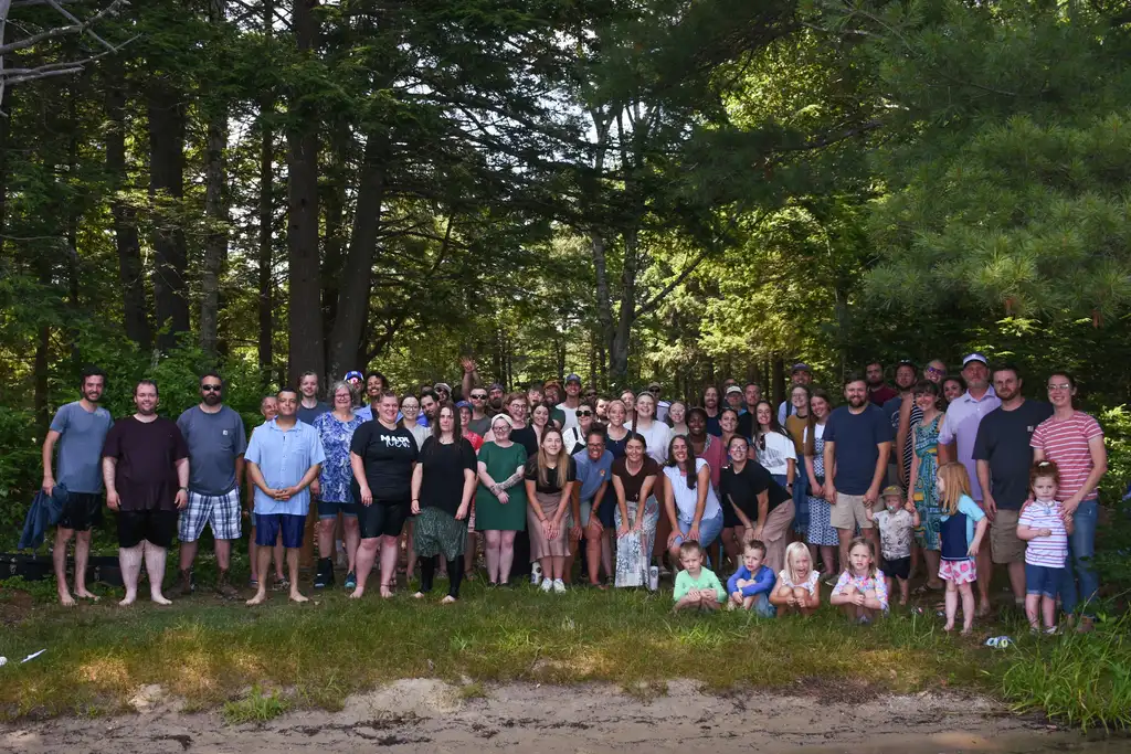 The His Mansion community, dozens of adults and children, gathered for a group photo among tall pines in summer